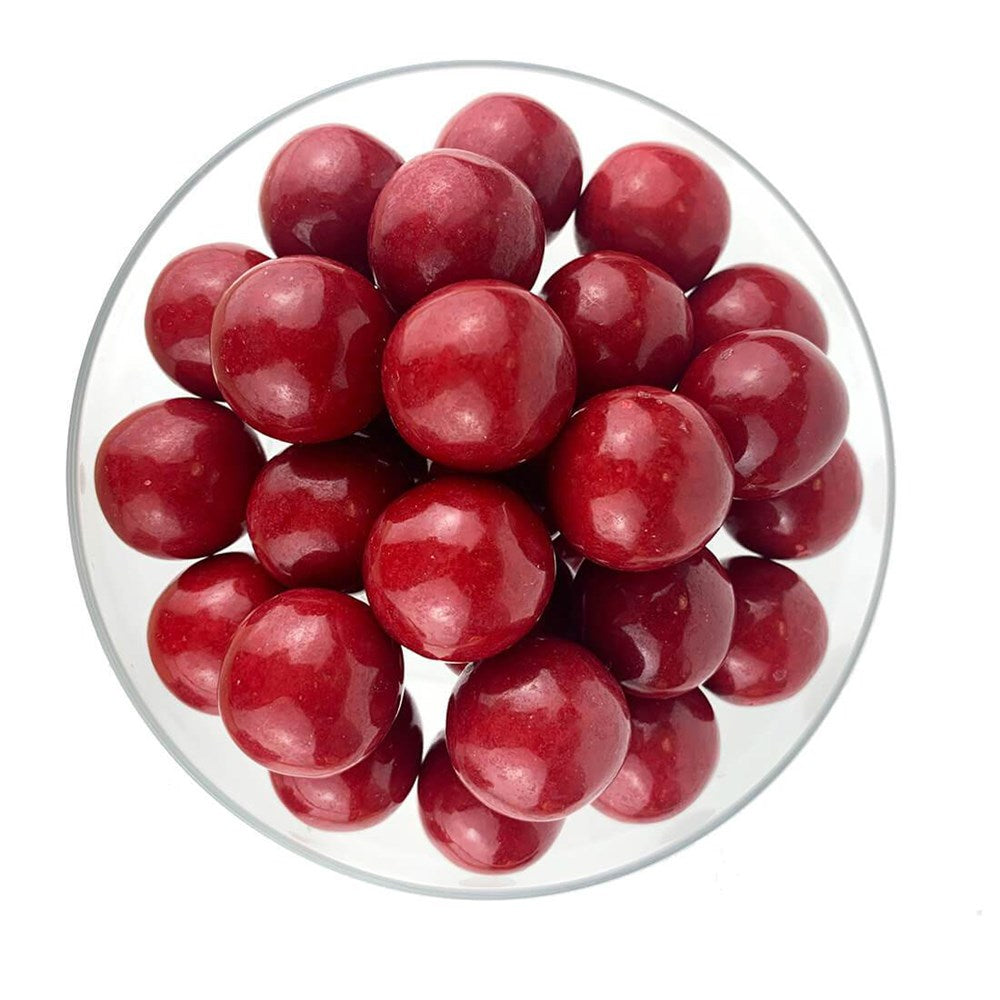 Glossy, round red gumballs piled together inside a clear, shallow bowl.