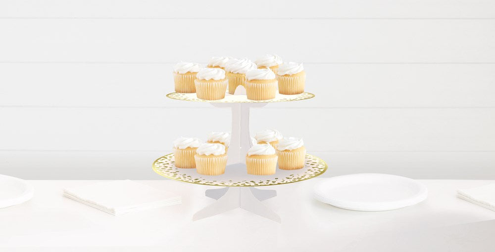 Two-tier white cupcake stand with gold polka dots, holding vanilla cupcakes with white frosting.