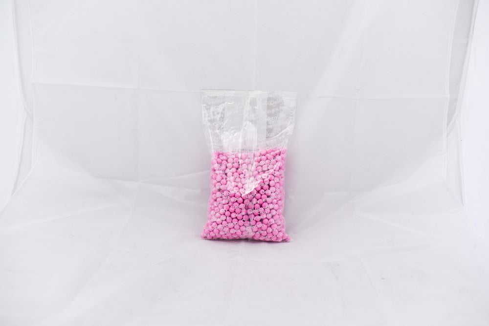 Clear plastic bag filled with small light pink round pellets on a white background.