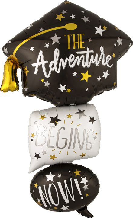Black foil graduation cap-shaped balloon with gold tassel and "The Adventure" text, stacked with white square balloon.
