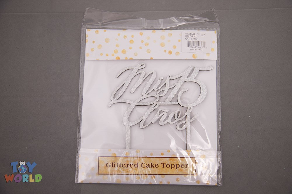 Silver glittered cake topper with "Mis Quinces" cursive text on two sticks.