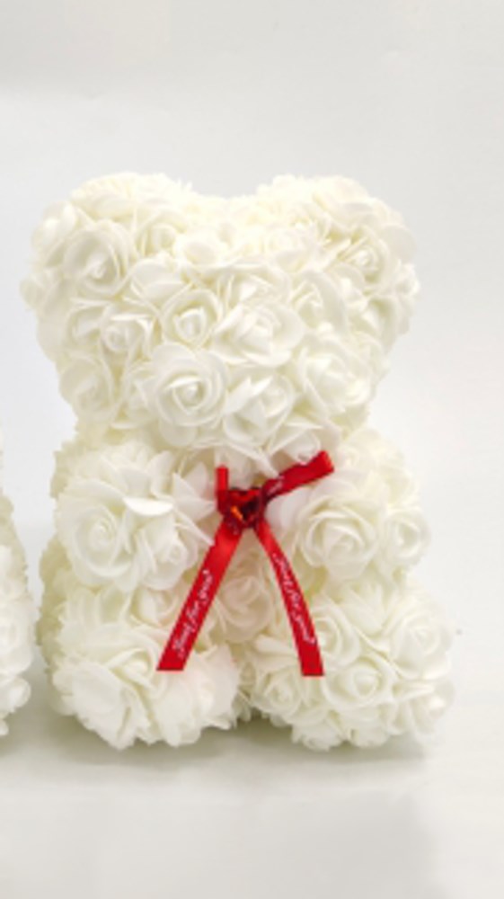 White teddy bear made of foam roses with a red satin ribbon bow around its neck.