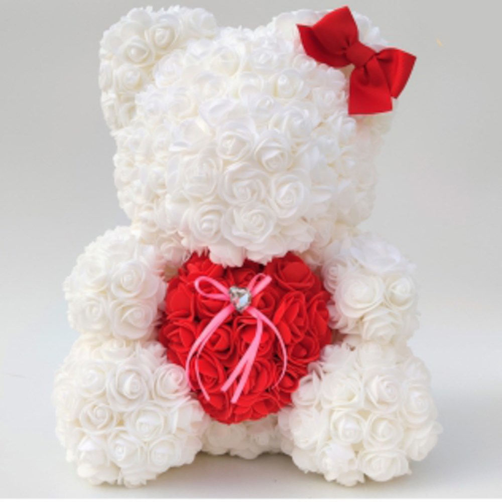 White plush bear made of foam roses holding a red heart with a pink bow, adorned with a red bow on its ear.