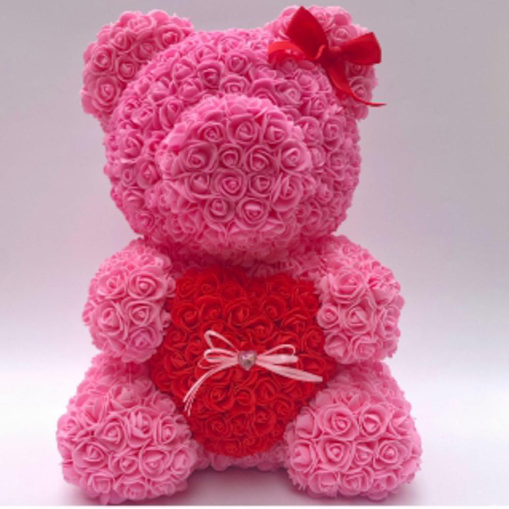 Pink teddy bear made of foam roses holding a red heart with a small white bow and a red ribbon on its head.