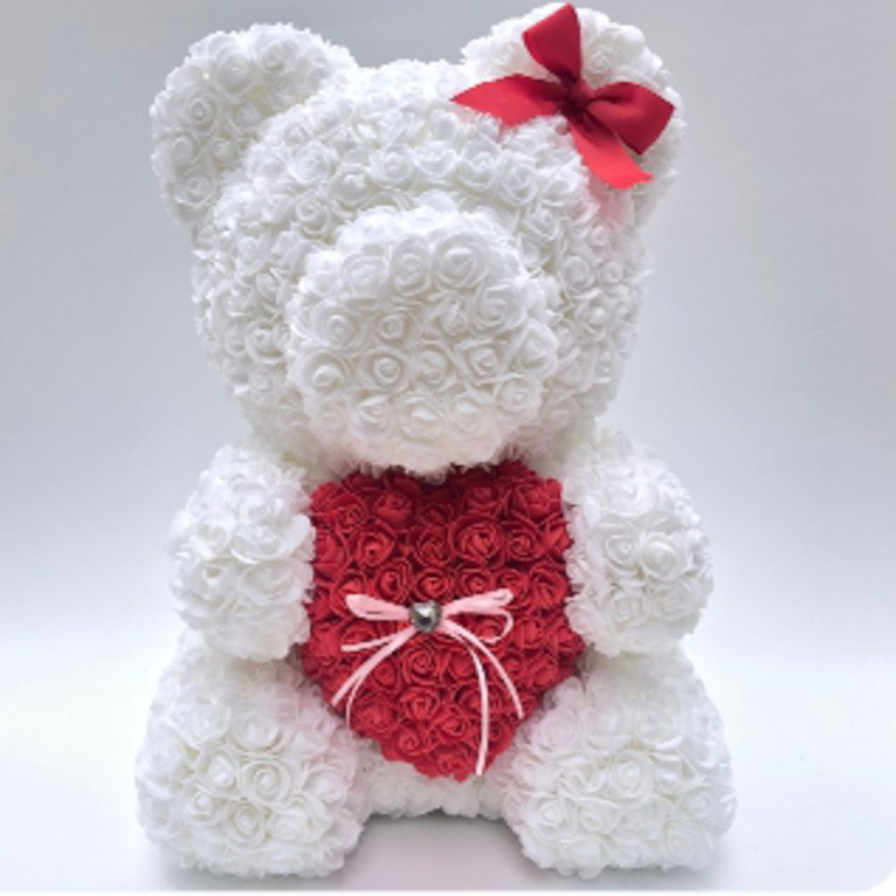 White teddy bear made from foam roses holding a red heart-shaped foam rose bouquet with a red bow on its head.