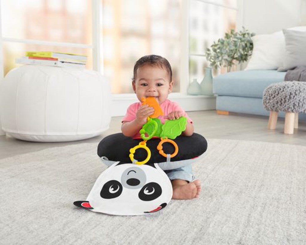 White and black panda-shaped soft tummy wedge with a baby holding green and orange teething toys sitting behind it.