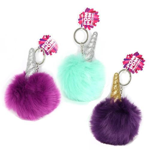 Three fluffy pom pom keychains in purple, turquoise, and dark purple, each topped with a glittery unicorn horn in silver or.