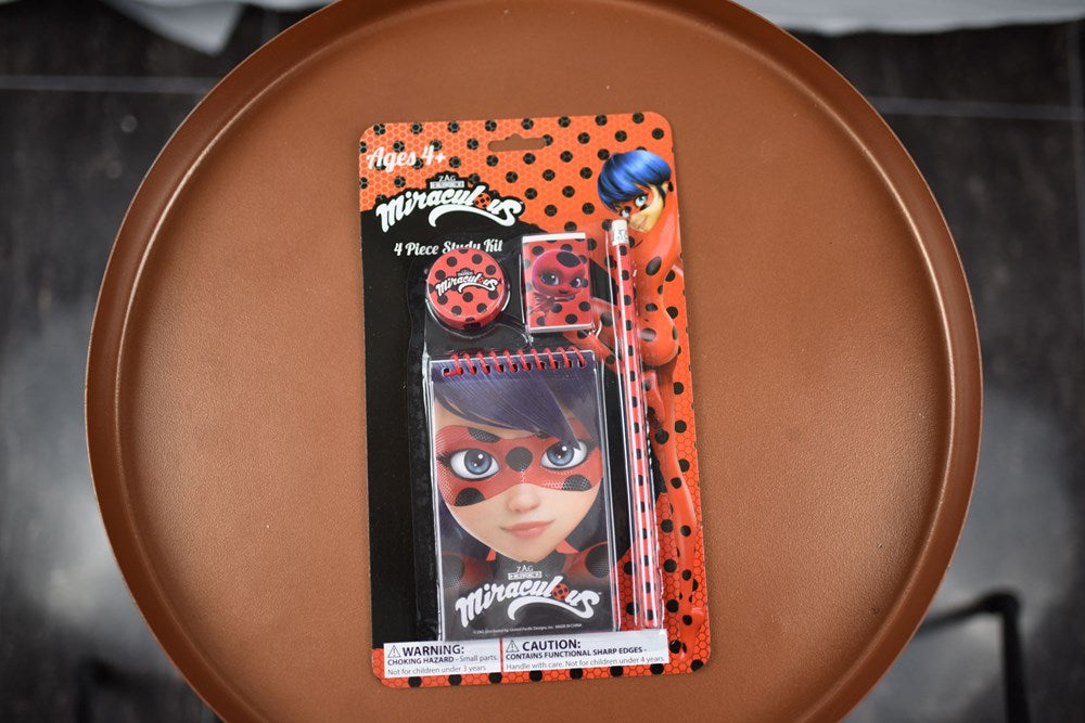 Red and black Miraculous Ladybug-themed 4-piece study kit with pen, ruler, eraser, and sharpener in polka dot packaging.