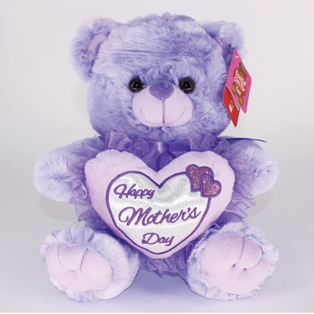Lavender plush teddy bear holding a heart pillow embroidered with “Happy Mother’s Day” and decorative bows.