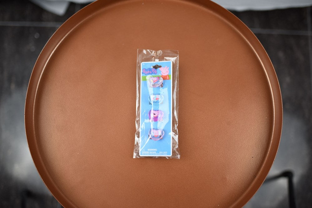 Set of four colorful Peppa Pig-themed plastic rings in clear packaging on brown surface.