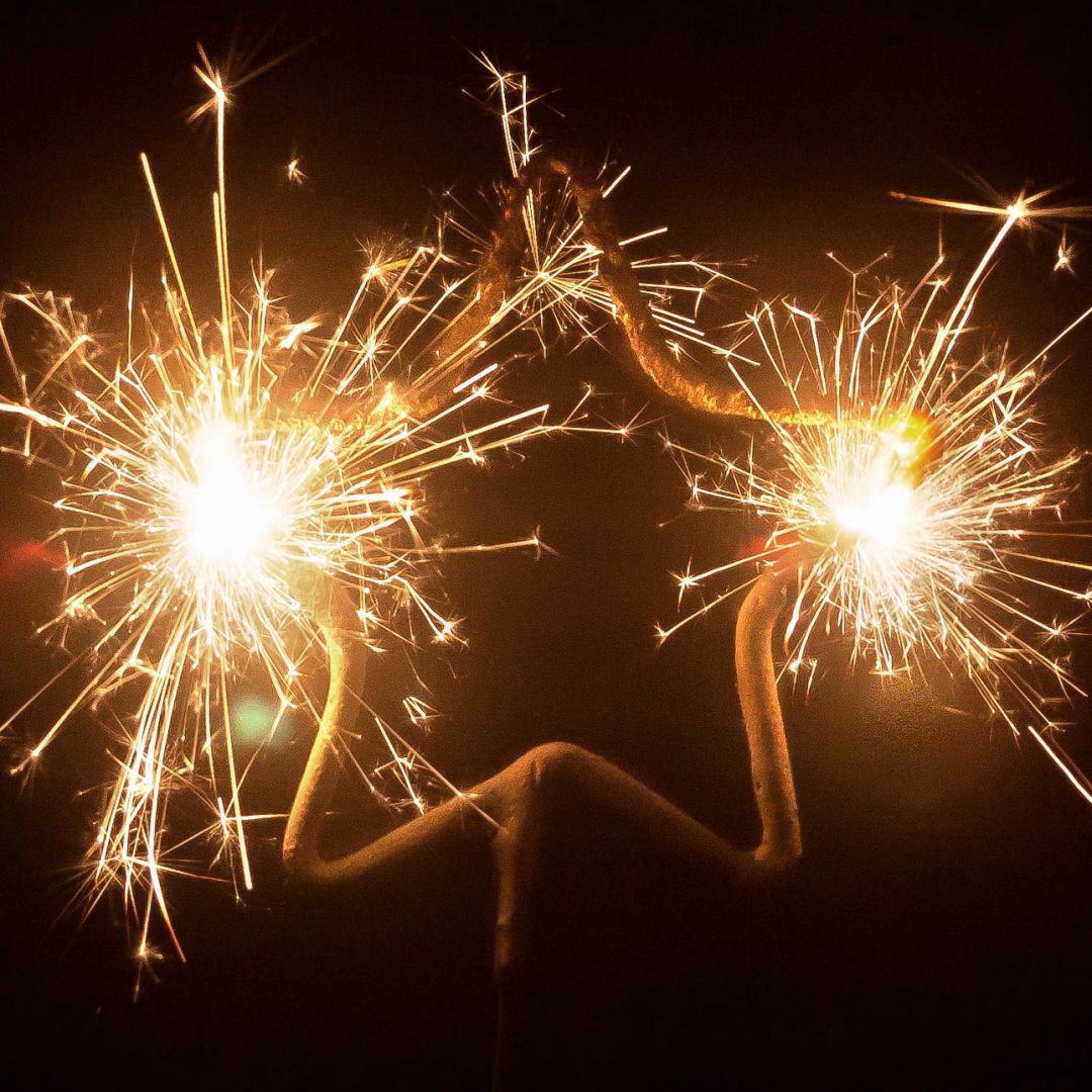 Three lit star-shaped sparklers glowing brightly with golden sparks against a dark background.