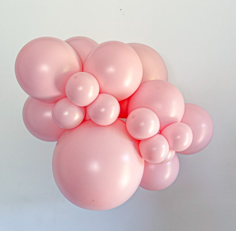 Cluster of shiny pink latex balloons in various sizes, arranged closely together.