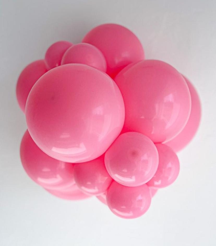 Cluster of glossy pink latex balloons in various sizes forming a spherical arrangement.