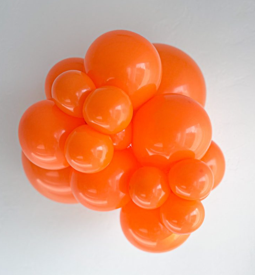 Cluster of shiny orange latex balloons in various sizes, inflated and arranged closely together.