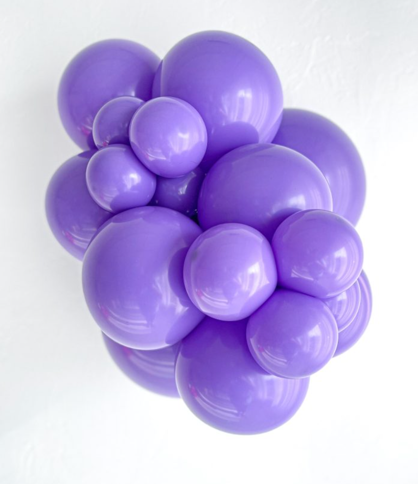 Cluster of shiny lavender purple latex balloons in various sizes tightly grouped together.