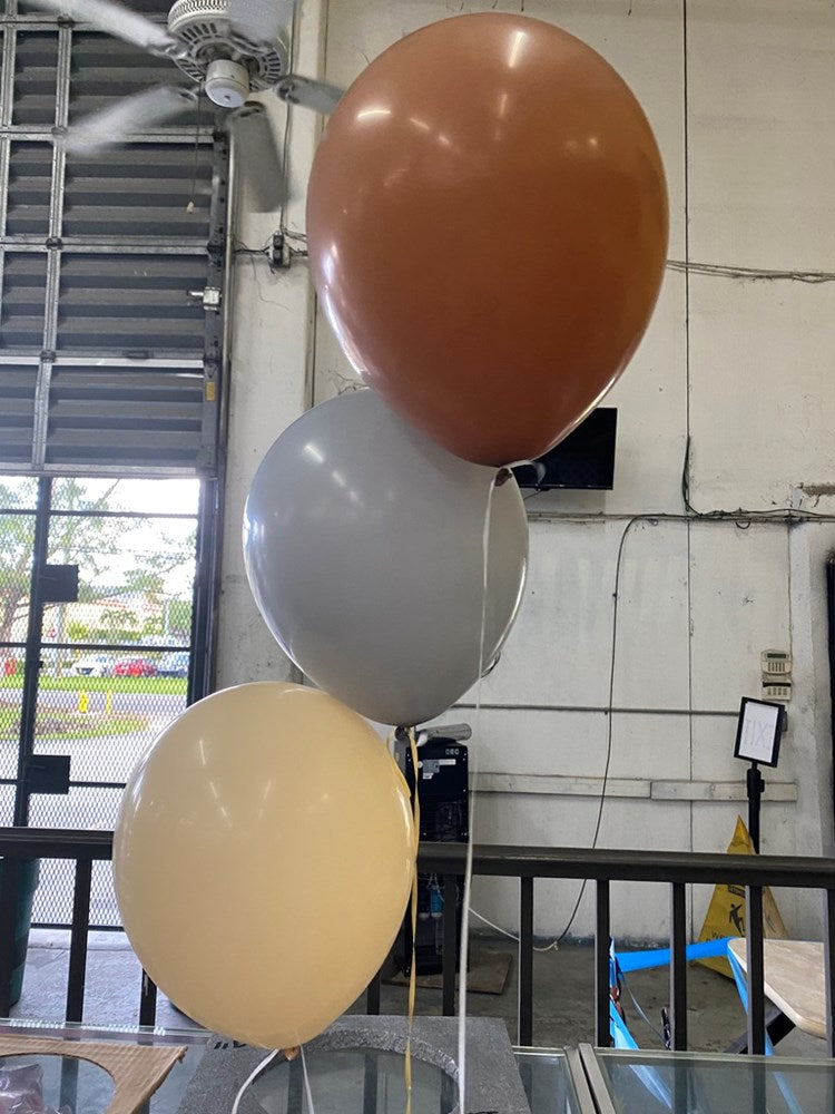 Set of three beige, light gray, and cream 12-inch latex balloons inflated and tied with white strings, indoor industrial.