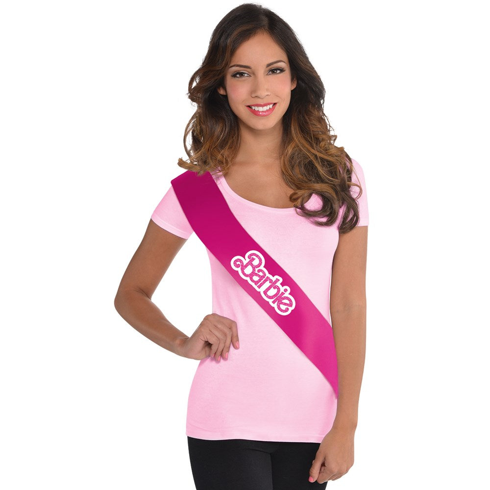 Bright pink satin sash with white "Barbie" logo, worn diagonally across a light pink shirt.