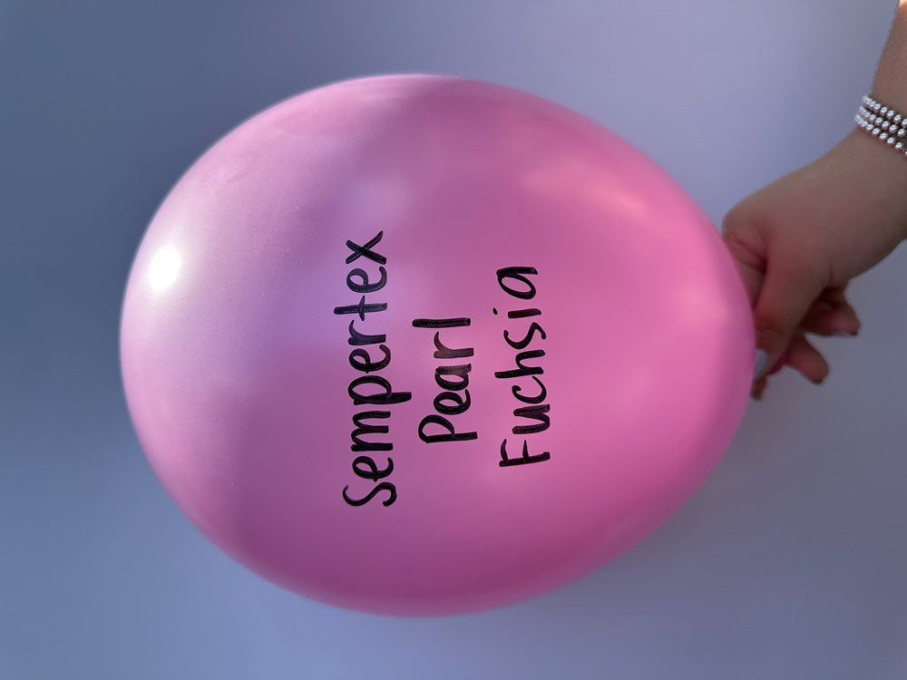 Single 5-inch round latex balloon in pearl fuchsia pink with a shiny finish, held by a hand.