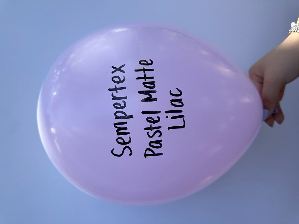 Pastel matte lilac 5-inch round latex balloon inflated and held by hand against a blue background.