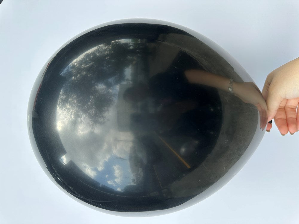 Glossy black 11-inch round latex balloon inflated and held by hand against a white background.