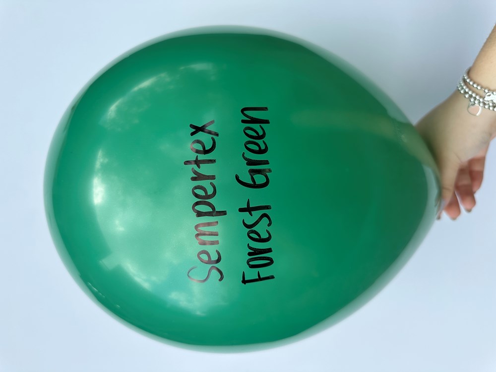 Glossy forest green latex balloon inflated, hand holding the tied end, black text printed on surface.