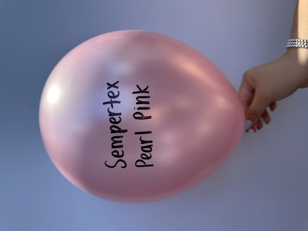 Pearl pink latex balloon inflated, smooth shiny surface, held by hand on light blue background.