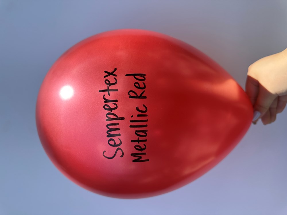 Shiny metallic red latex balloon inflated and held by hand with Sempertex Metallic Red text printed on it.