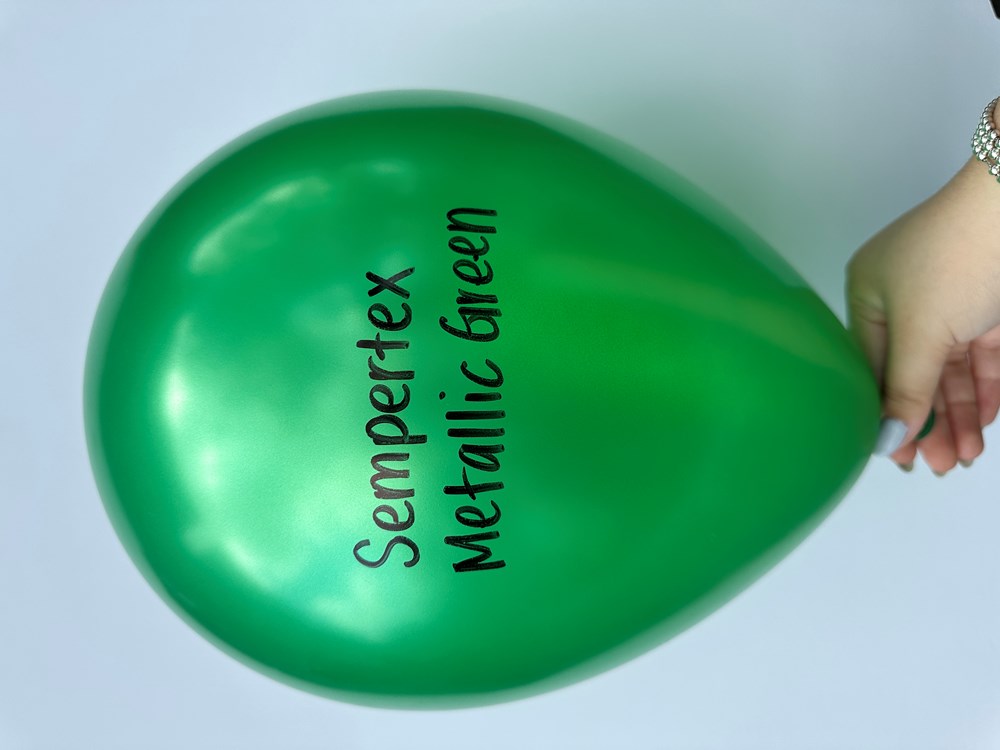 Shiny metallic green latex balloon inflated, held by hand against plain background.