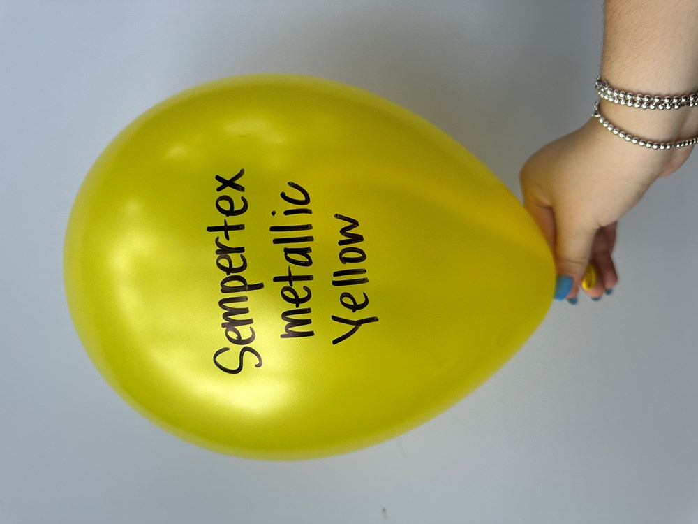 Bright metallic yellow latex balloon with black text, 11-inch round shape, held by hand.