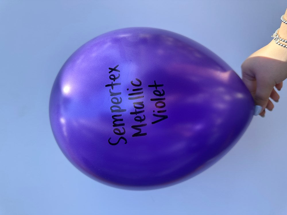 11-inch shiny metallic violet latex balloon with black text printed on it, held by hand.