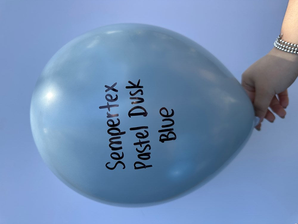 Matte pastel dusk blue latex balloon inflated, held by a hand on a light blue background.