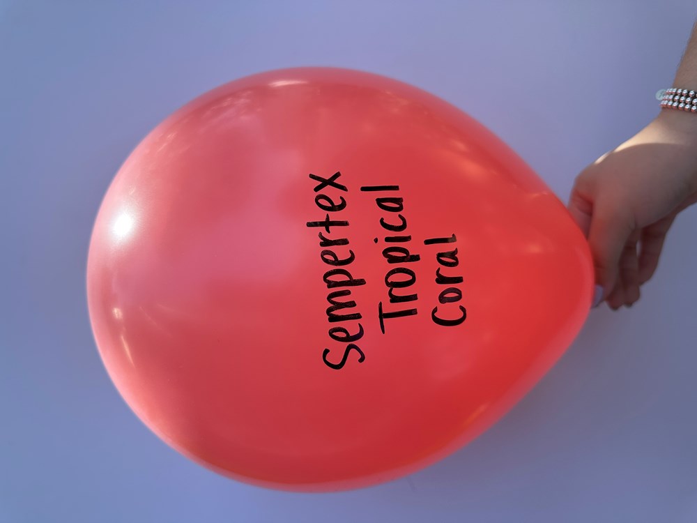 Glossy 11-inch tropical coral latex balloon with black Sempertex Tropical Coral text, held by hand.