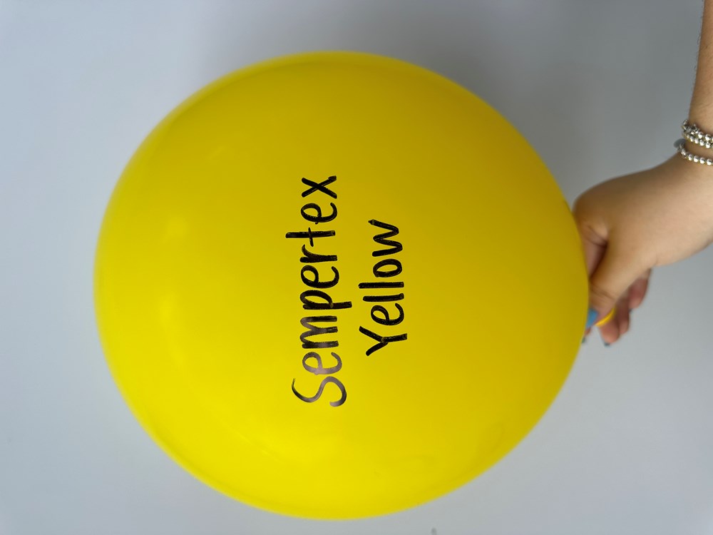 Bright yellow 18-inch round latex balloon with Sempertex Yellow text, hand holding knot.