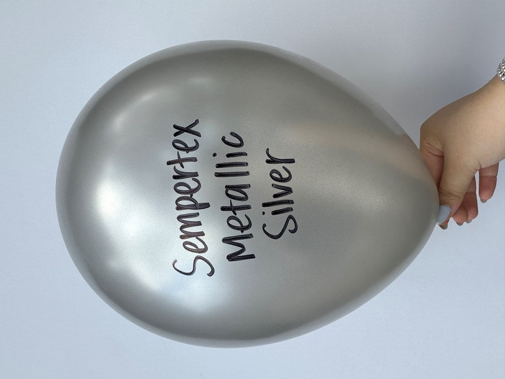 Metallic silver latex balloon inflated, teardrop shape with black printed text, held by hand.