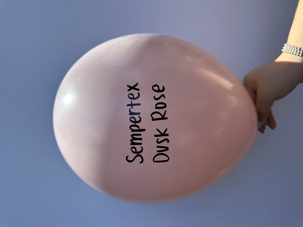 Round latex balloon in soft pastel dusk rose pink, inflated and held by a hand, printed with "Sempertex Dusk Rose" in black.