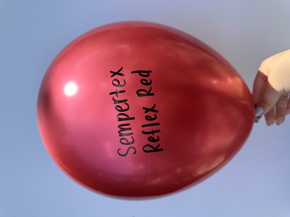 Shiny, reflex red latex balloon inflated, held by hand against a blue background.