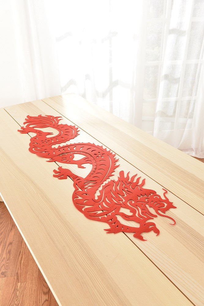 Red dragon design on a beige fabric table runner with scalloped edges.