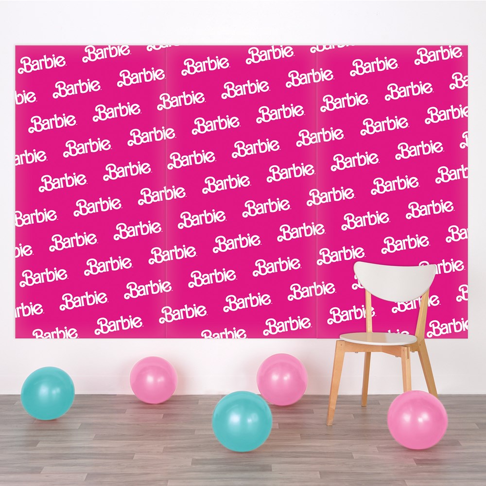 Pink rectangular backdrop with repeating white Barbie logos, surrounded by pink and blue balloons and a wooden chair with.
