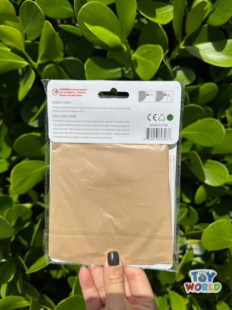 Square caramel-colored foil balloon in sealed clear packaging held against green foliage background.