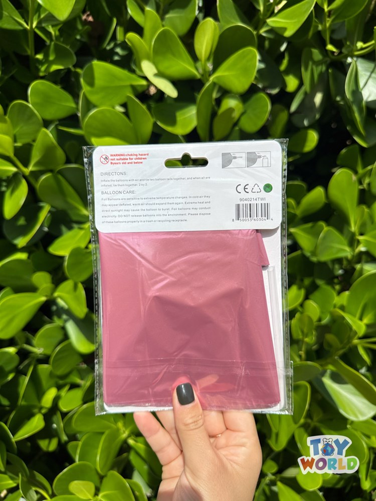 Folded baby pink star burst foil balloon in clear plastic packaging held against green leaves background.