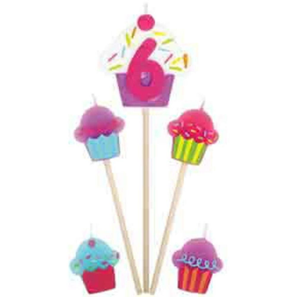 Number 6 candle with pink frosting and sprinkles on wooden pick, surrounded by colorful cupcake picks with frosting and.