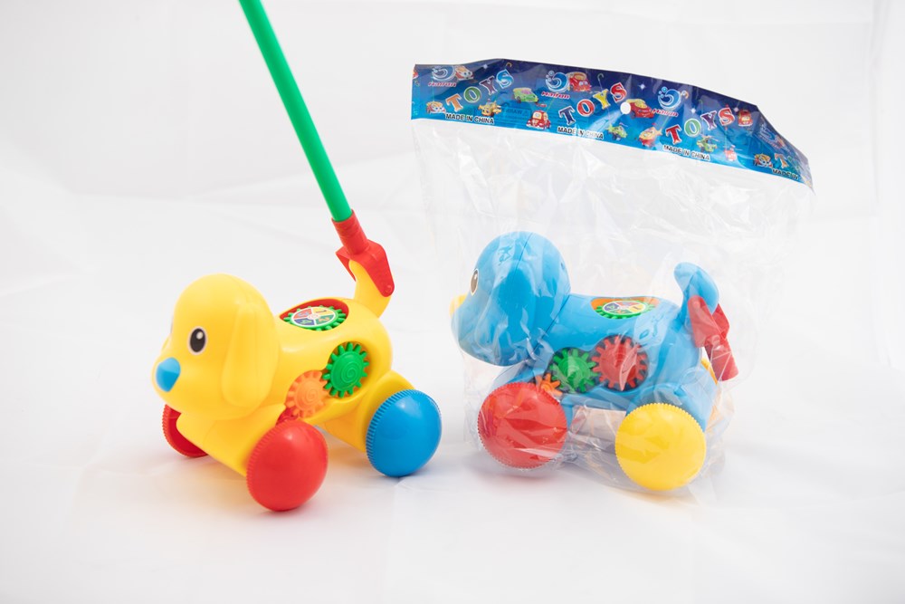 Yellow rolling dog toy with red wheels and green stick, colorful gears on sides; blue version wrapped in plastic.