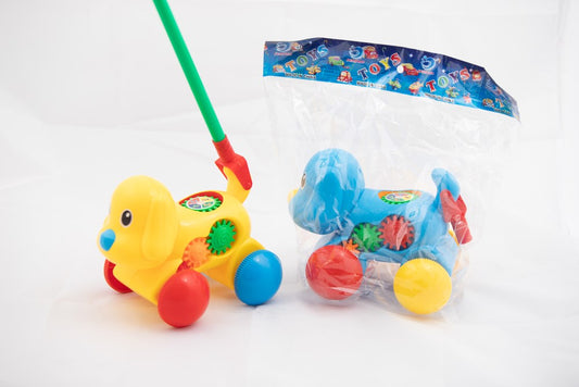Yellow rolling dog toy with red wheels and green stick, colorful gears on sides; blue version wrapped in plastic.