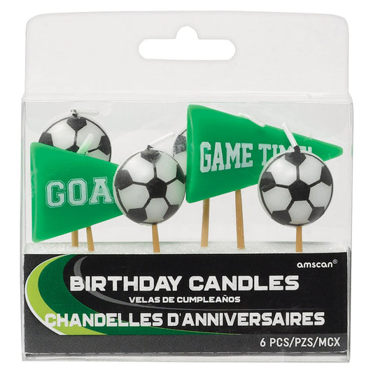 Six colorful birthday candles shaped like soccer balls and green pennant flags with "GOAL" and "GAME TIME" text, on wooden.