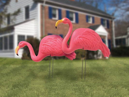 Two bright pink plastic flamingo lawn ornaments with curved necks and yellow-tipped beaks on thin metal stakes.