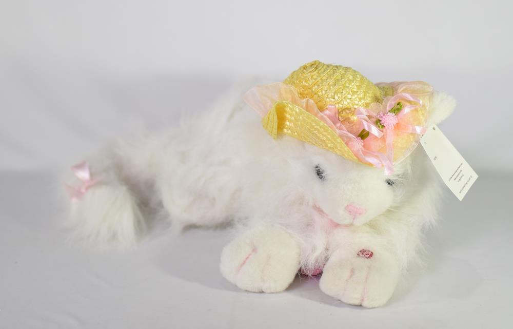 White plush cat with pink nose and paws wearing yellow woven hat with pink flowers, 16 inches long.