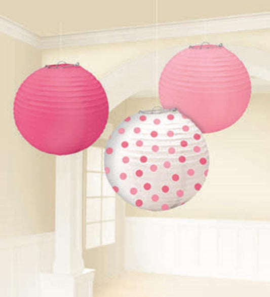Three round paper lanterns in shades of pink, one solid light pink, one solid dark pink, and one white with pink polka dots,