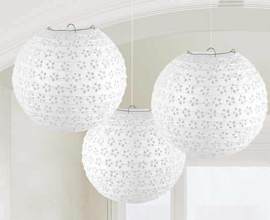 Three white round paper lanterns with floral eyelet cutout patterns hanging indoors.