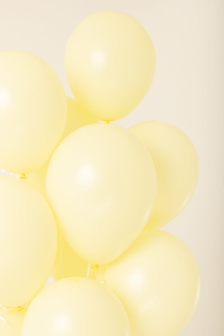 Cluster of six pale yellow 11-inch latex balloons inflated with helium against a neutral background.