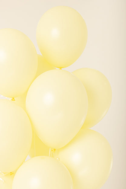 Cluster of six pale yellow 11-inch latex balloons inflated with helium against a neutral background.